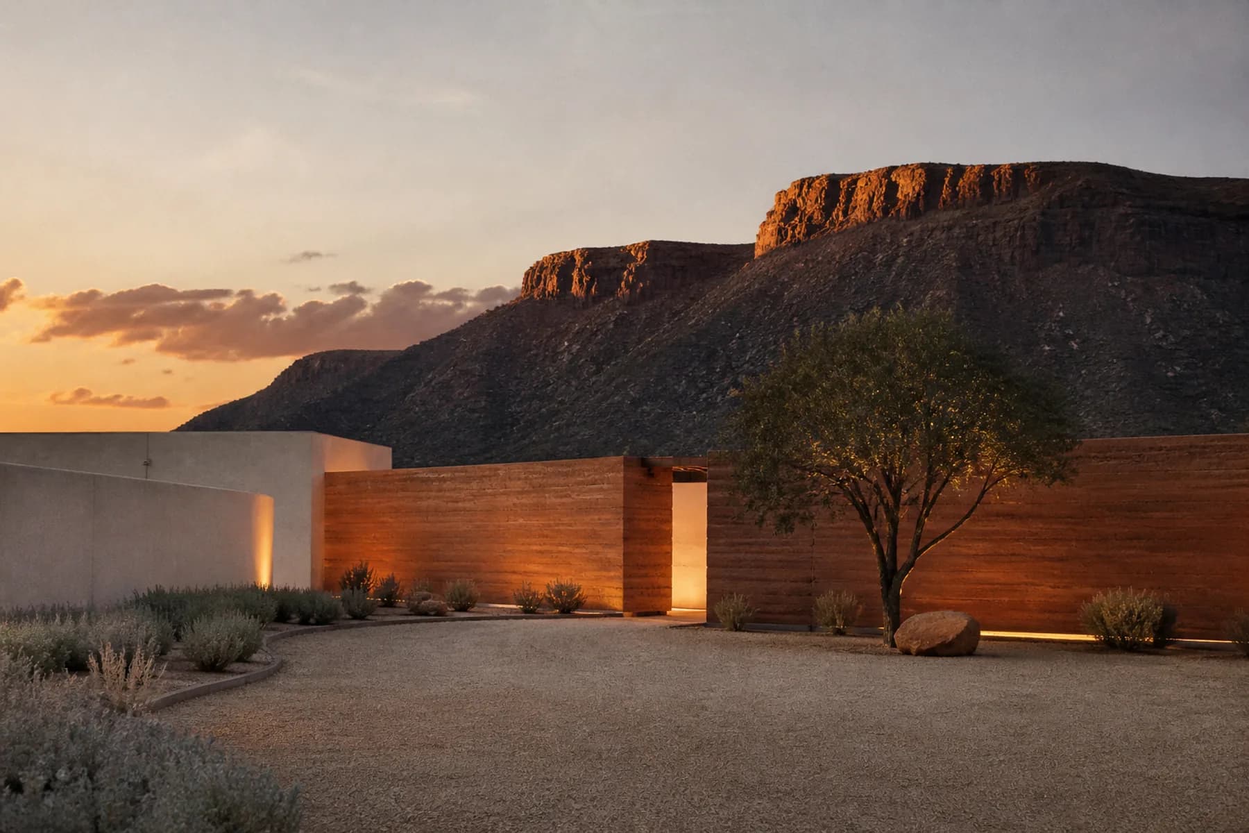 An arrival court at dusk, a rammed-earth wall with a narrow opening glowing warm from within