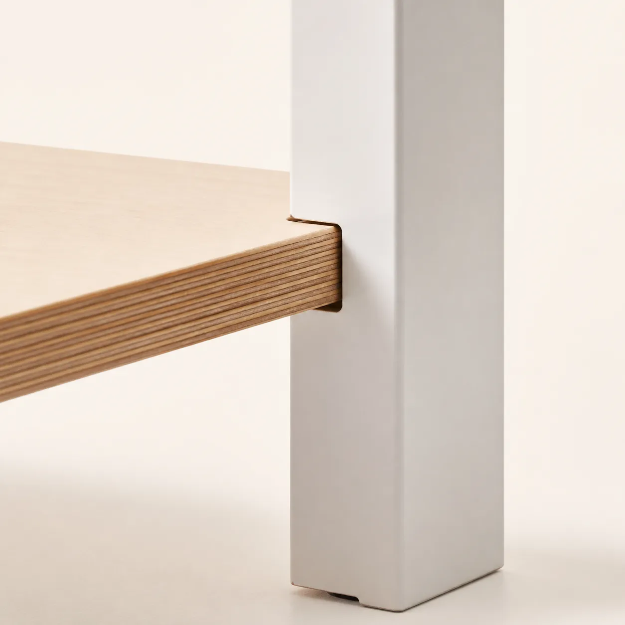 Macro view of a birch plywood tenon sliding into a matching slot in a white powder-coated steel upright