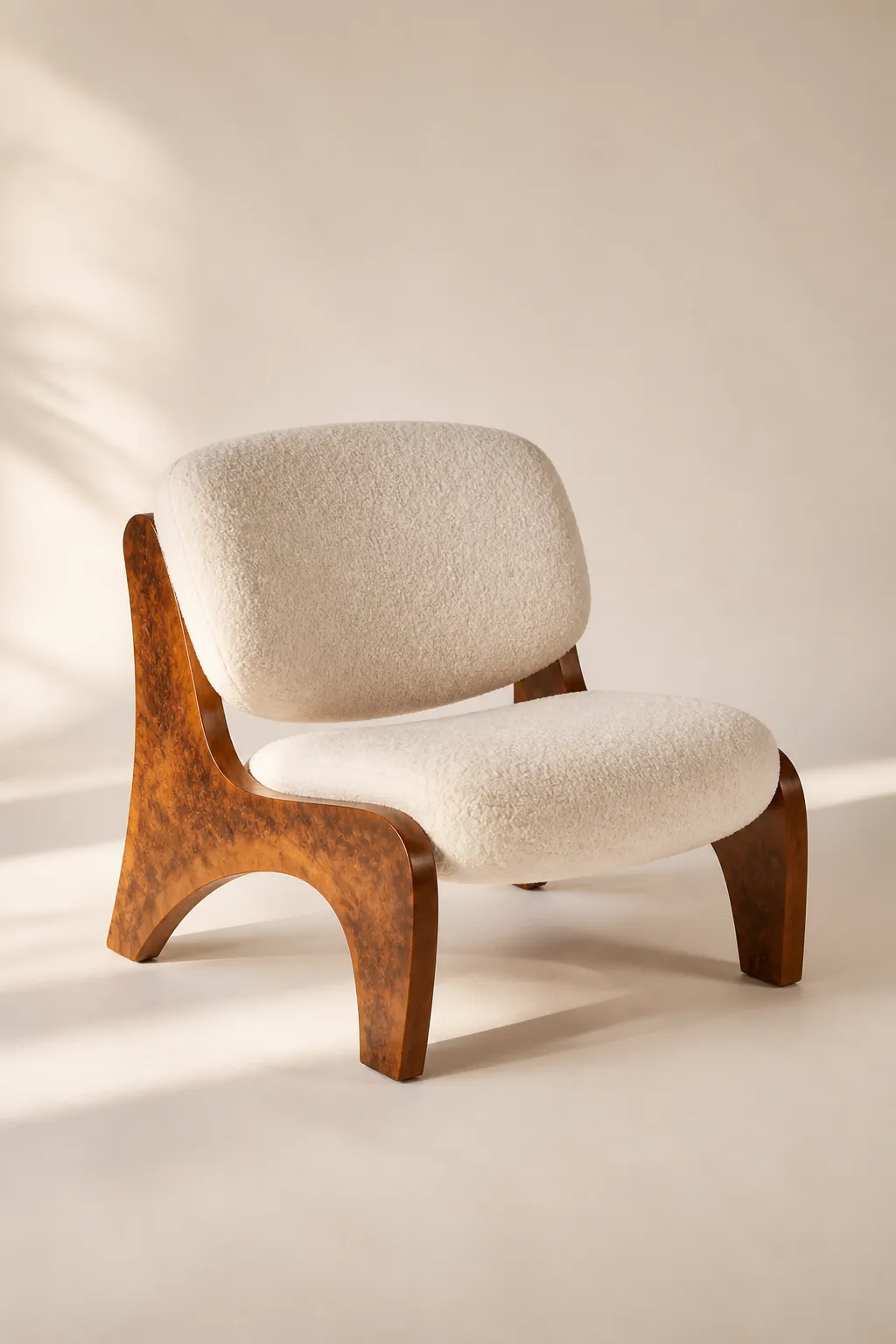 A low lounge chair with a curved burl wood frame and cream bouclé upholstery on a warm cream background.