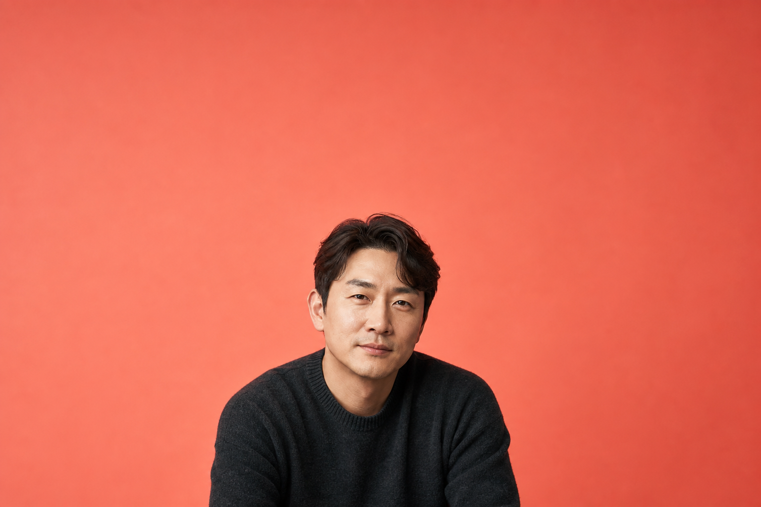 코랄 배경 앞에서 차분히 정면을 보는 남성, 위쪽은 빈 코랄 공간