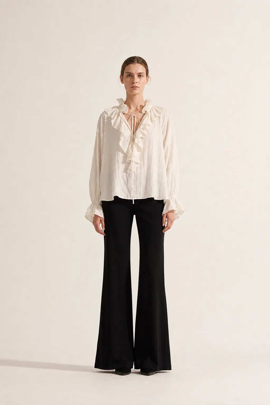 Look 01 — an airy white ruffle blouse over black flared trousers, photographed from the front
